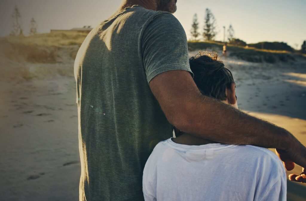 A man walking on a beach with his arm around a child